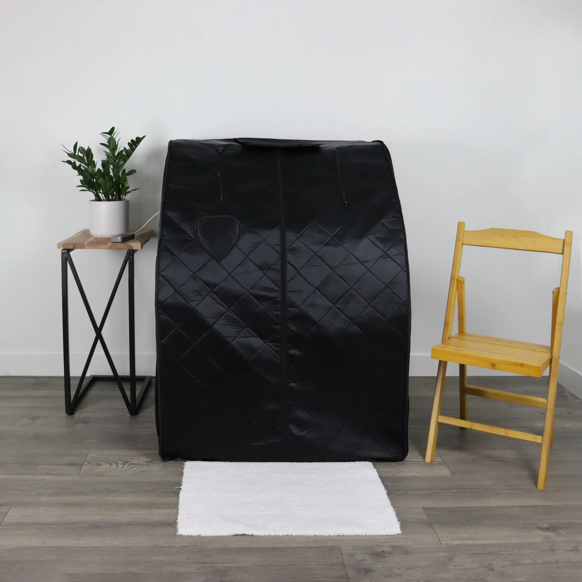 The portable infrared sauna made by UltraLux Health, in a living room next to a table with a plant, and bamboo chair.